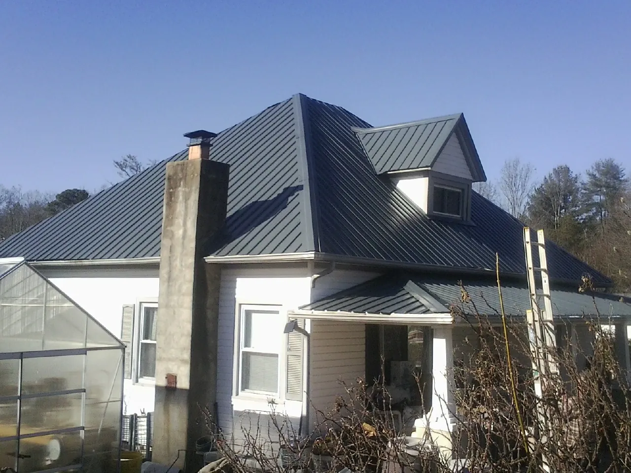 Dark blue standing seam metal roof on a white farmhouse with dormer — Slate & Tile Roof Repair by Roofing Brothers in Pleasant Lake
