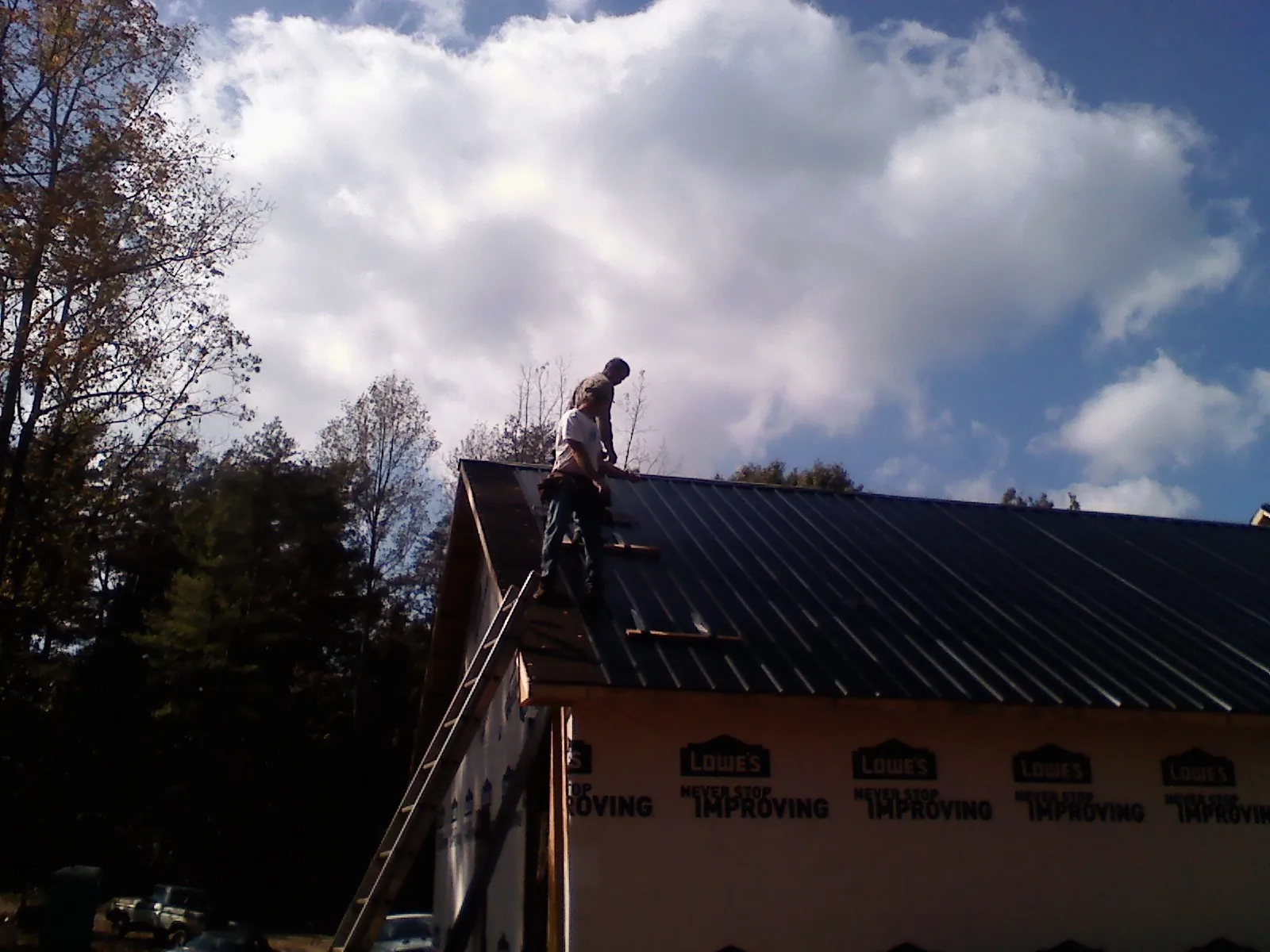 Roofer fastening dark metal panels high against a cloudy sky, from a Roof Inspection job in Pleasant Lake