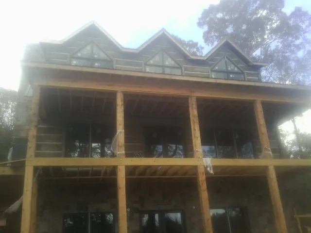 Dormers and porch framing on a large log home under construction — Roof Coating work by our crew in Pleasant Lake